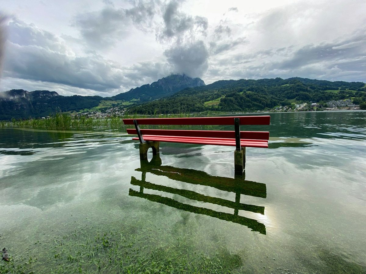 Rote Holzbank am Seeufer von Horw, dahinter der Pilatus über dem Vierwaldstättersee