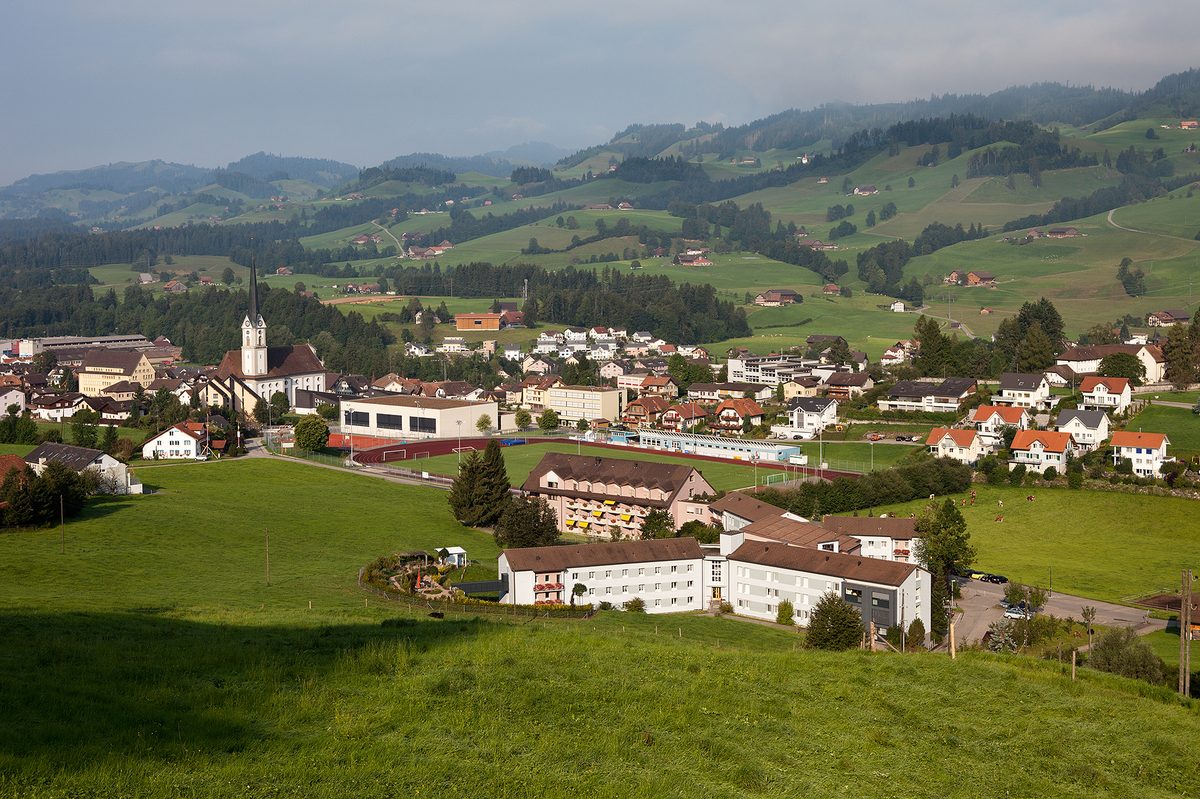 Schüpfheim am Morgen, mit Pfarrkirche und Sportplatz vor den Hügeln des Entlebuchs