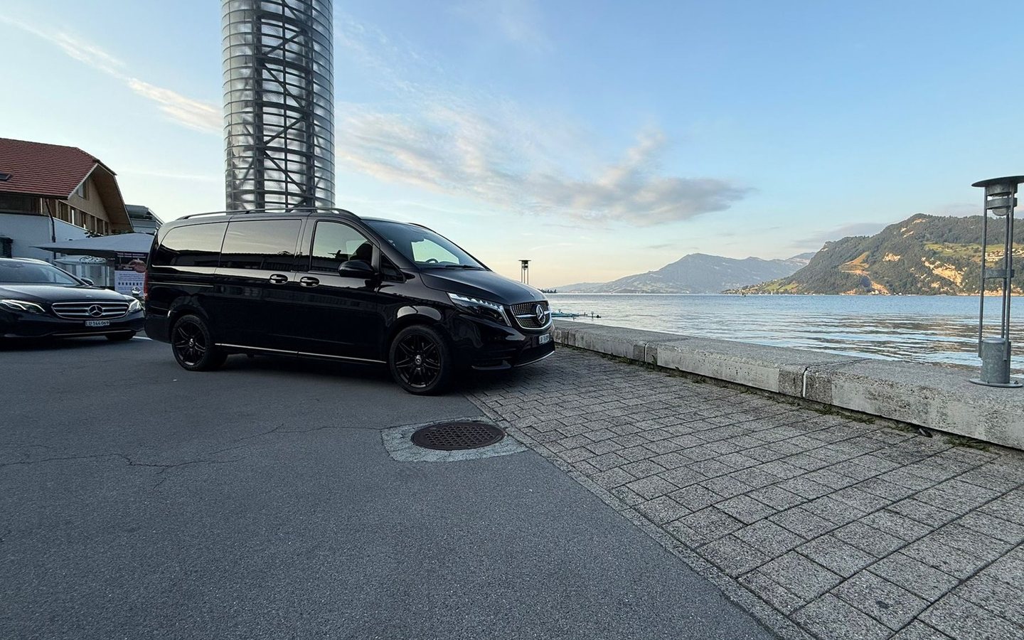 Schwarze Mercedes V-Klasse von Luzerner Taxi an der Uferpromenade vor See und Bergen